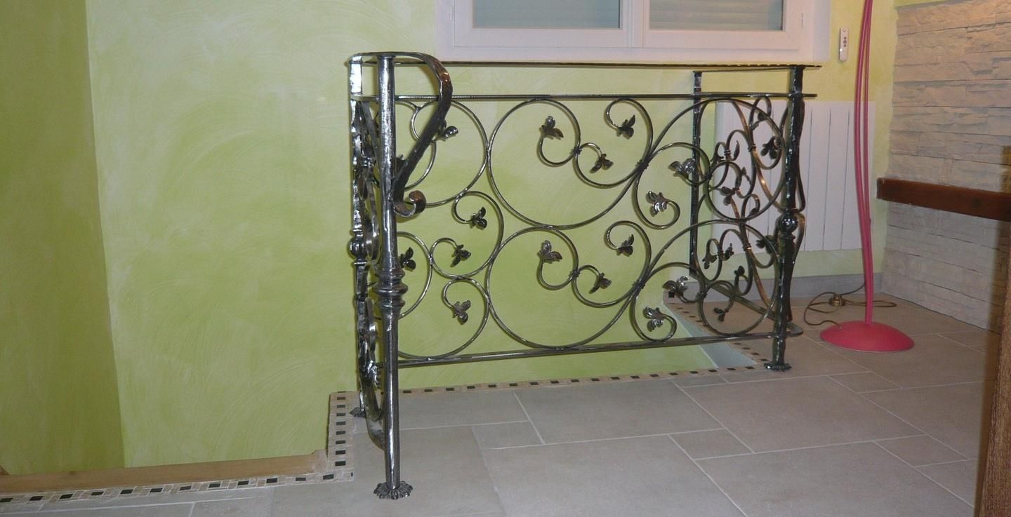 Rambarde en métal noir ornée le long d'un escalier ou d'un palier intérieur carrelé, à côté d'un mur et d'une fenêtre vert pâle