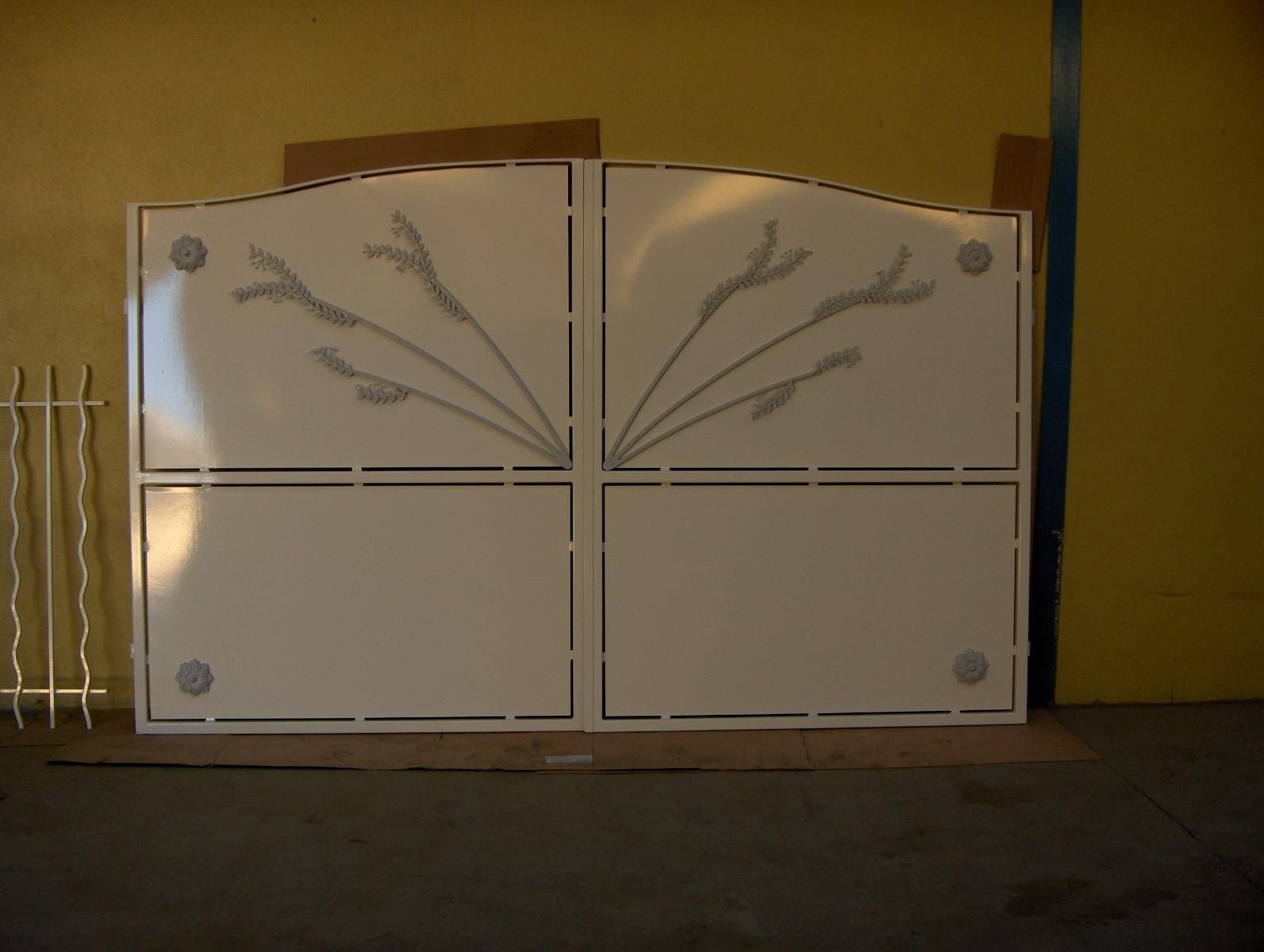 Portail métallique blanc fermé, orné de motifs de branches grises, appuyé contre un mur dans un espace intérieur sombre.