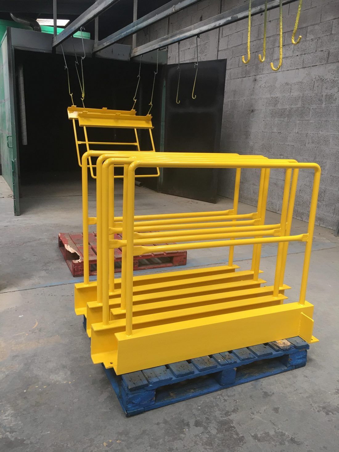 Des garde-corps métalliques jaunes sont empilés sur des palettes bleues dans une zone de stockage industrielle.