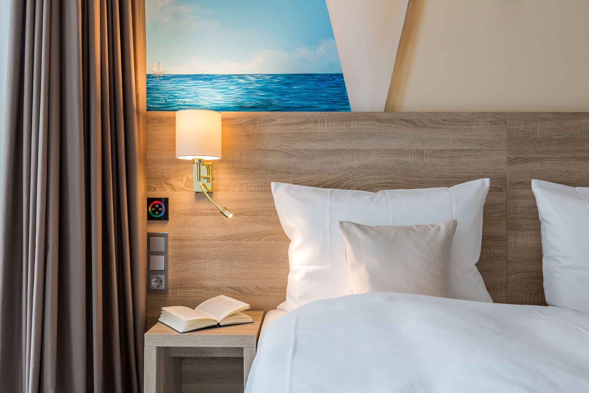 Schlafzimmer mit einem Bett, einem Nachttisch mit einem Buch, einer Lampe und einem Wandkunstbild mit Meeresmotiv.