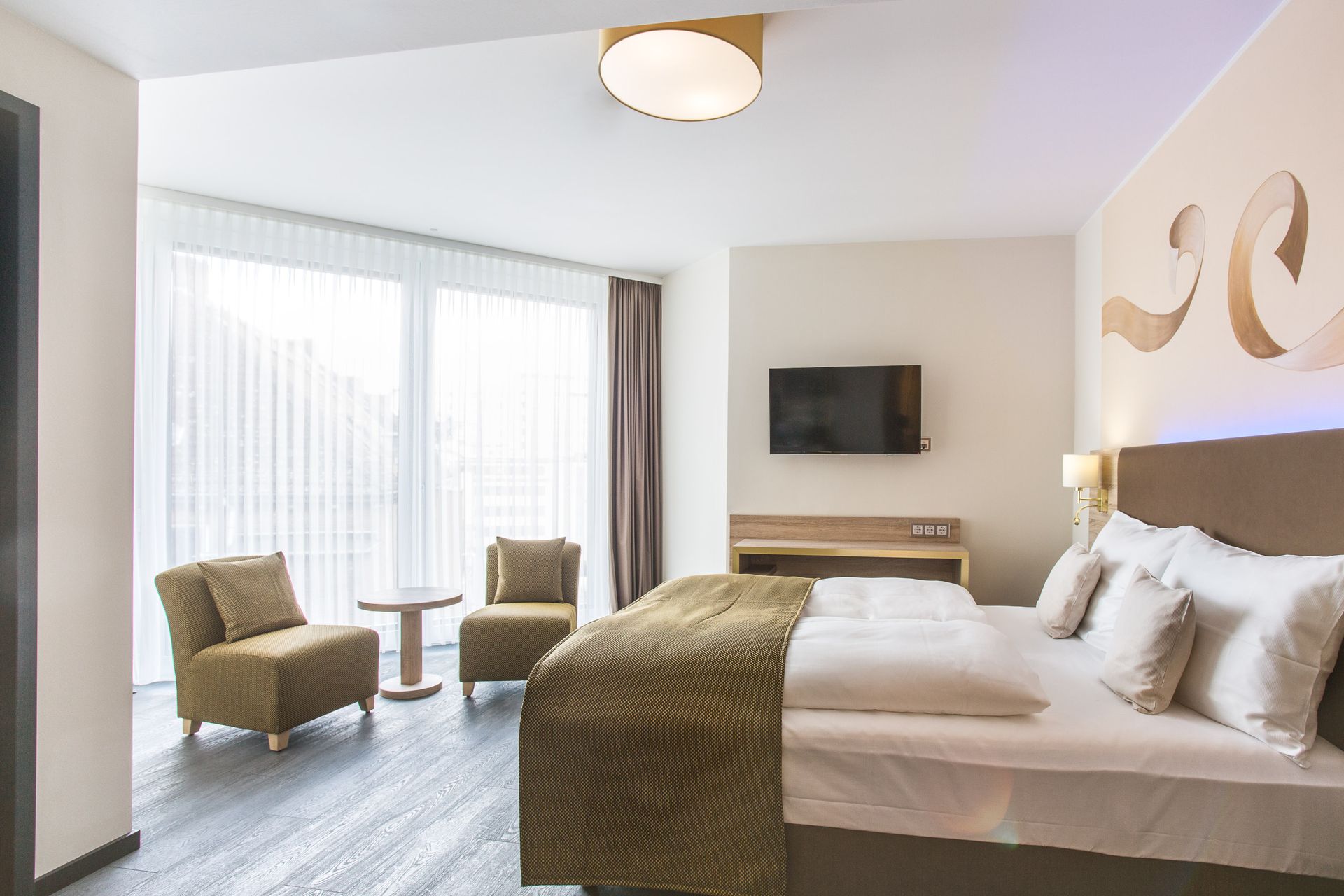 Hotelzimmer mit Bett, Stühlen und großem Fenster.