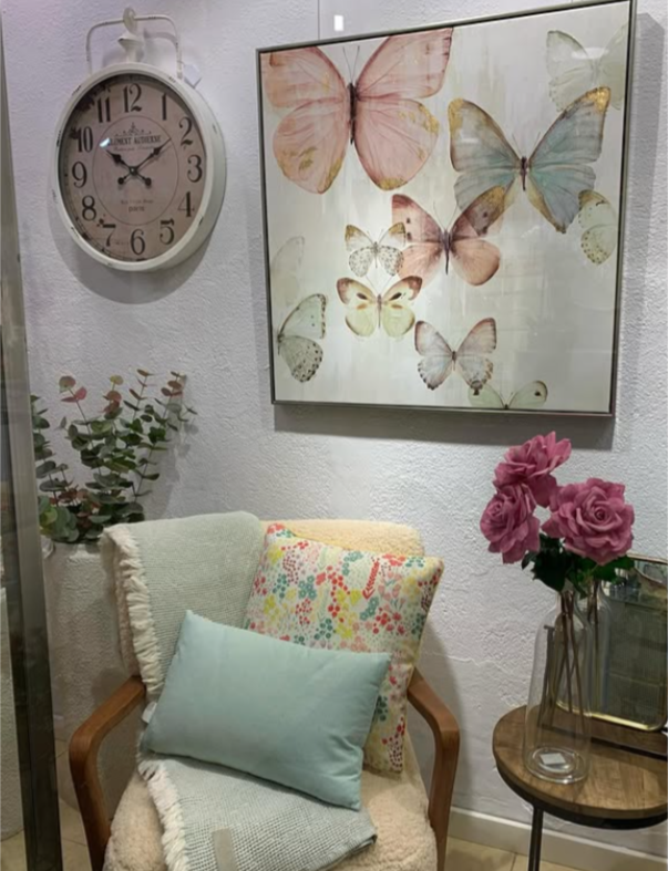 Una habitación con una silla, una mesa, un reloj y un cuadro de mariposas en la pared.