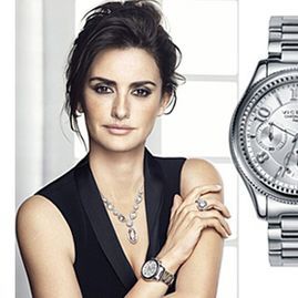 Una mujer que lleva un reloj y un collar está parada al lado de un reloj.