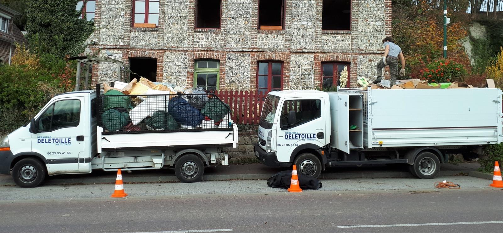 Des camions-bennes chargés de détritus devant une maison en brique.