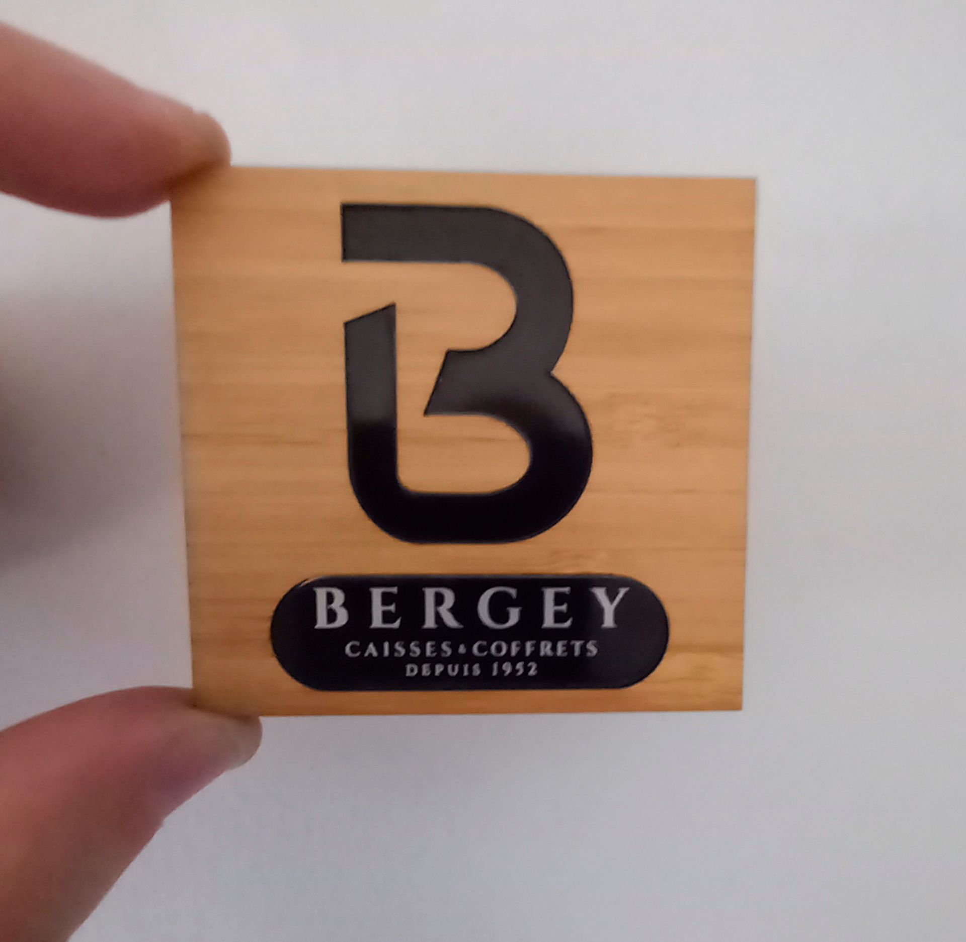 Une main tenant un bloc de bois carré avec un logo noir « B »