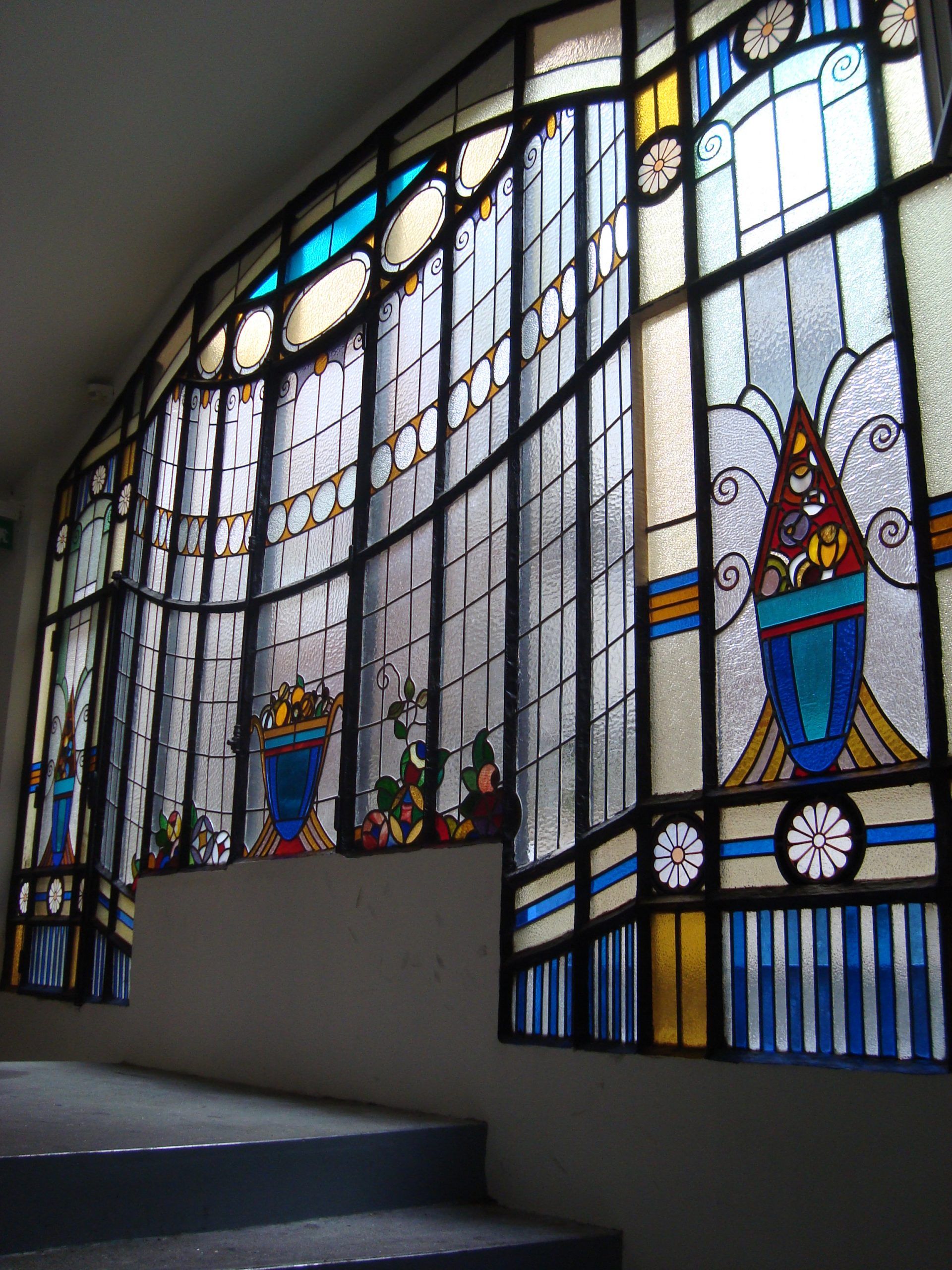 Vitrail de forme incurvée, orné de vases décoratifs bleus, dorés et blancs, le long d'un escalier.