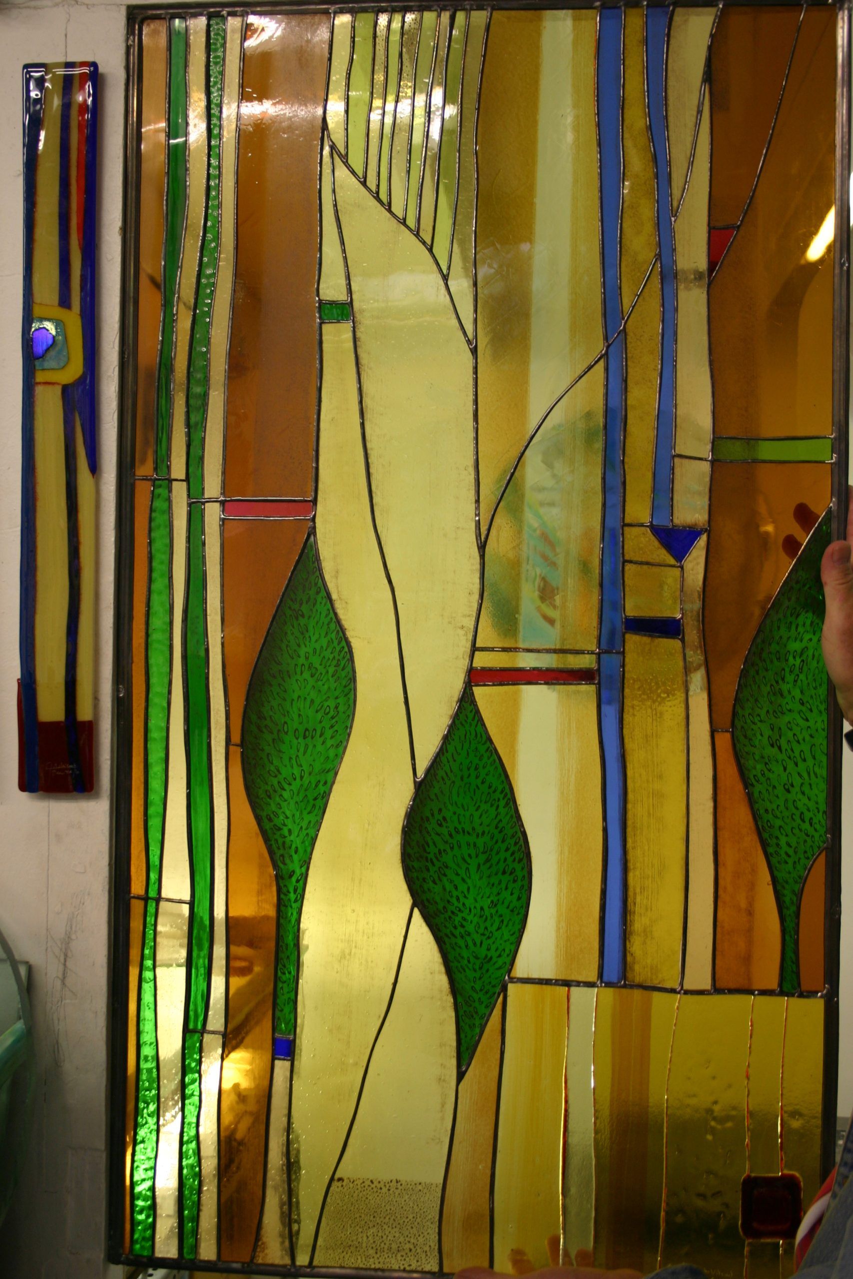 Vitrail à motif abstrait d'arbres verts sur fond jaune/or avec des touches de bleu.