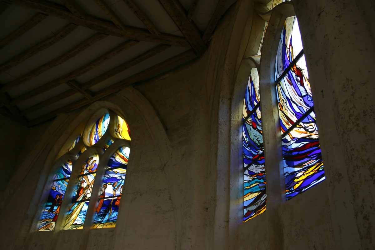Deux vitraux à l'intérieur d'un bâtiment en pierre, aux teintes bleues, jaunes et rouges.