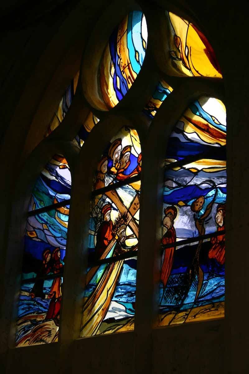 Vitrail représentant des personnages sur une barque au milieu de volutes bleues et jaunes, probablement une scène religieuse.