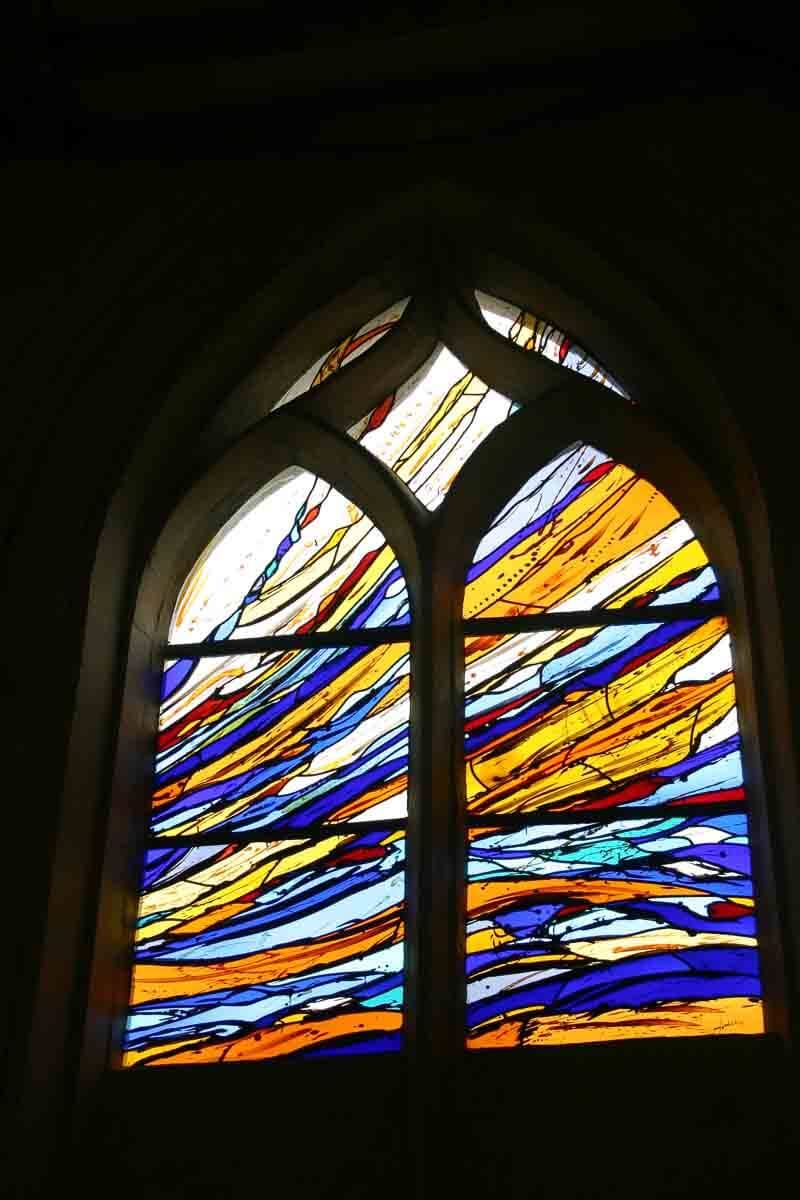 Vitrail orné d'un motif abstrait de rayures bleues, jaunes et orange sur fond sombre.