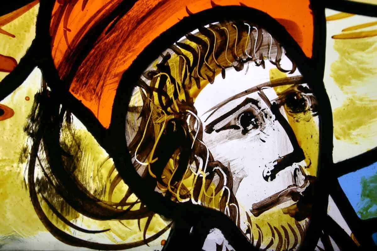 Portrait d'un homme en vitrail, de profil. Détails orange et jaunes, encadrement noir et expression pensive.