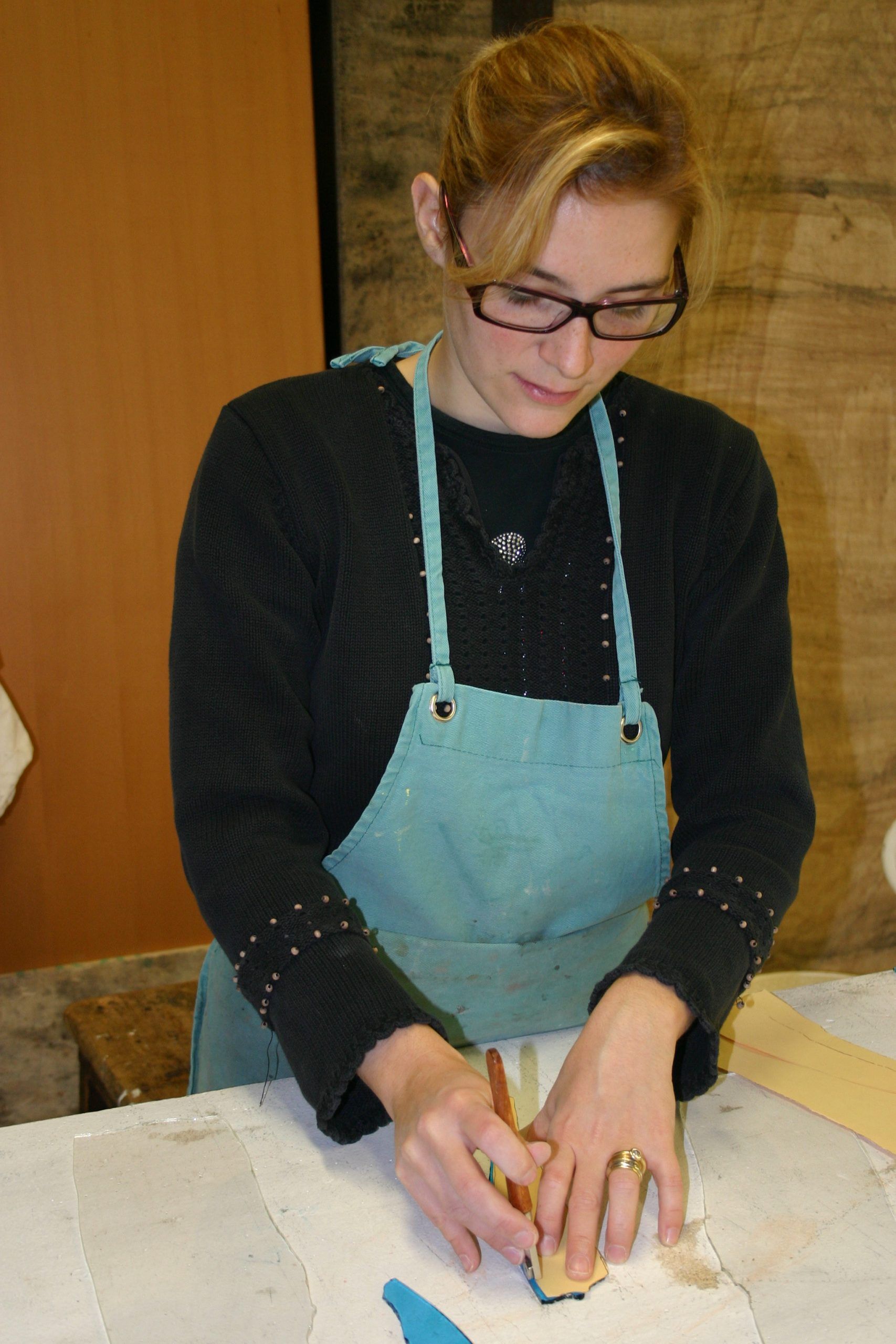 Femme portant des lunettes et un tablier travaillant avec un outil sur une surface blanche ; à l'intérieur.