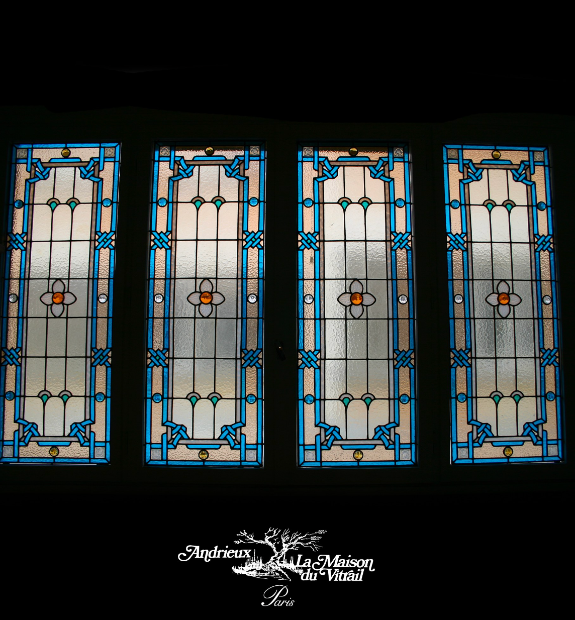 Quatre vitraux ornés de touches de bleu, de blanc et d'orange, se détachant sur un fond noir.