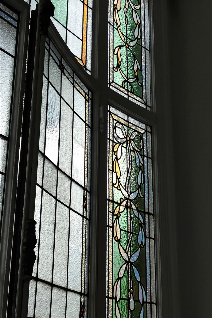 Vitrail ouvert. Motif floral vert et blanc, la lumière filtrant à travers la vitre.