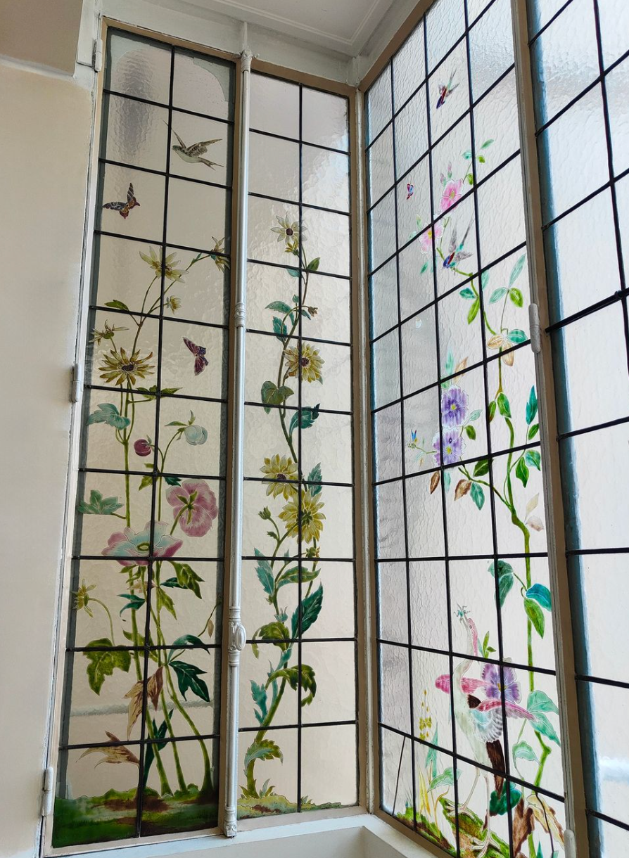 Vitrail orné de motifs floraux et d'oiseaux dans des tons de vert, de rose et de jaune.