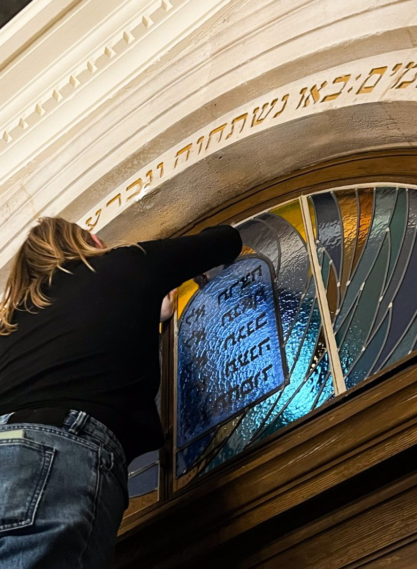 Une femme installe un panneau de vitrail avec un texte hébreu, probablement dans une synagogue.