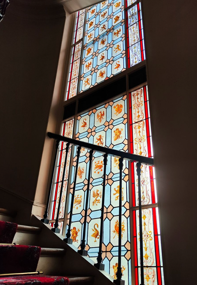 Vitrail sur un escalier, présentant des motifs orange et jaunes répétitifs, sur fond bleu, avec des bordures rouges.