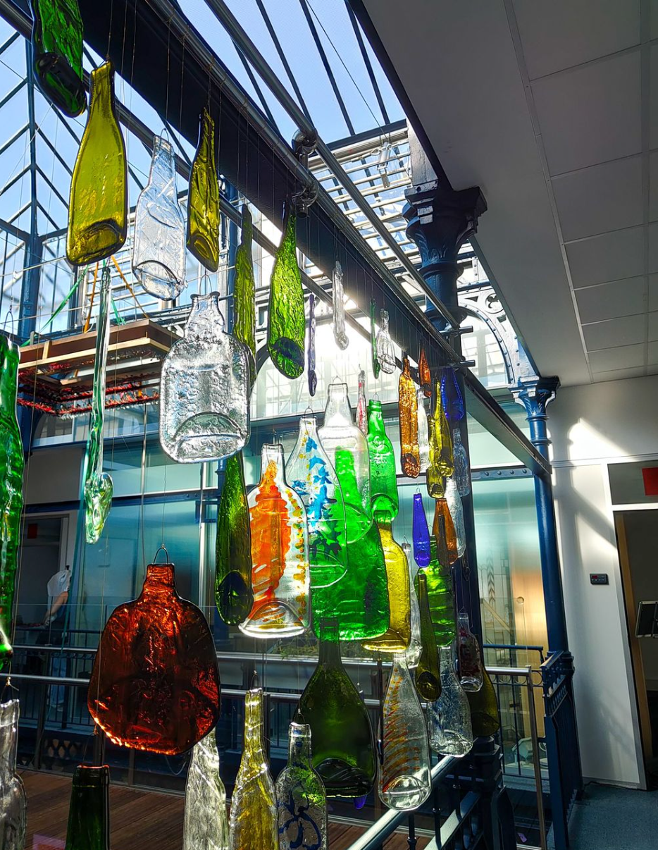 Des bouteilles en verre colorées suspendues à une structure métallique créent un élément décoratif à l'intérieur d'un bâtiment.