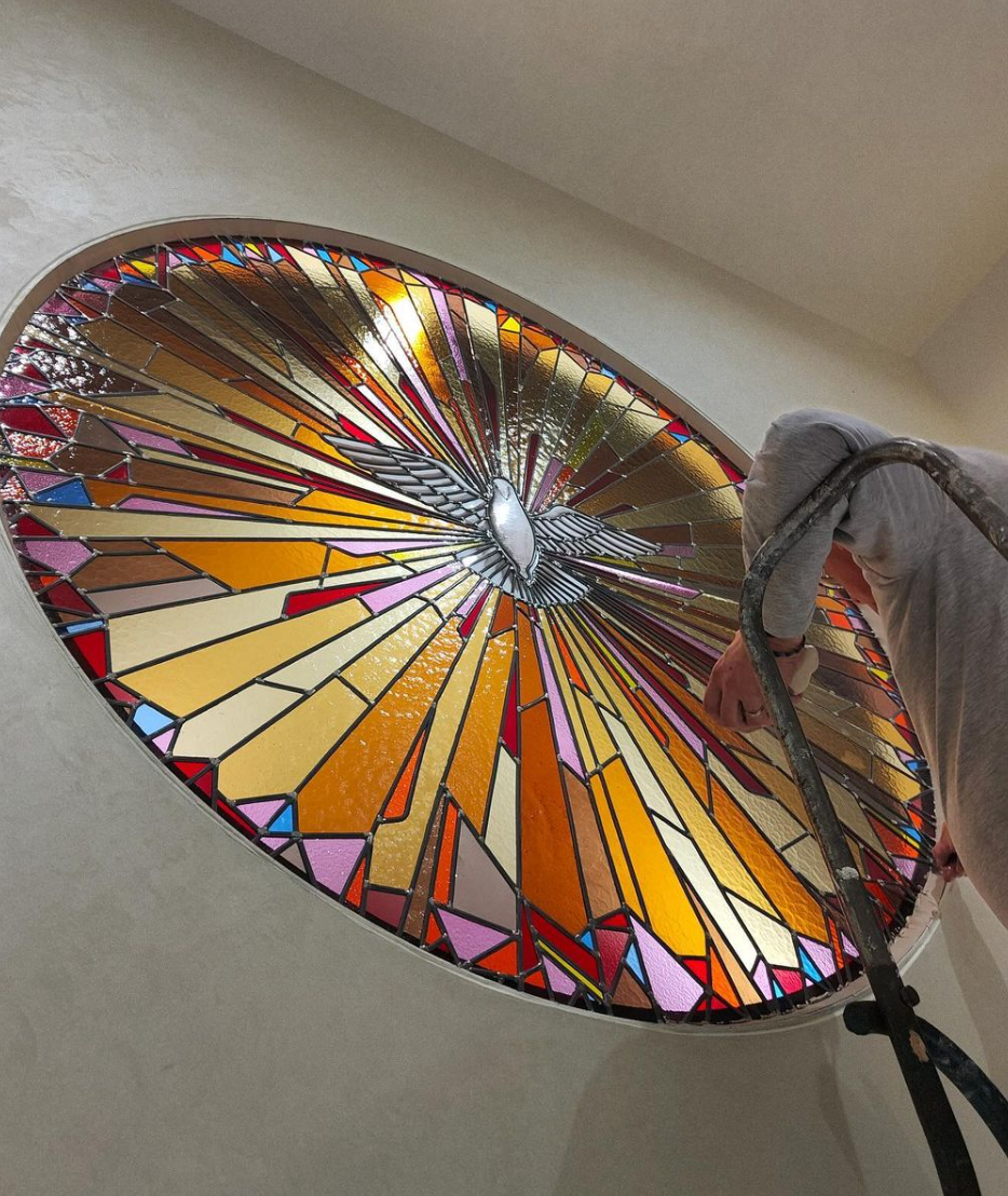 Vitrail ovale orné d'un motif de soleil rayonnant. Une main tient des ciseaux lors de l'installation.