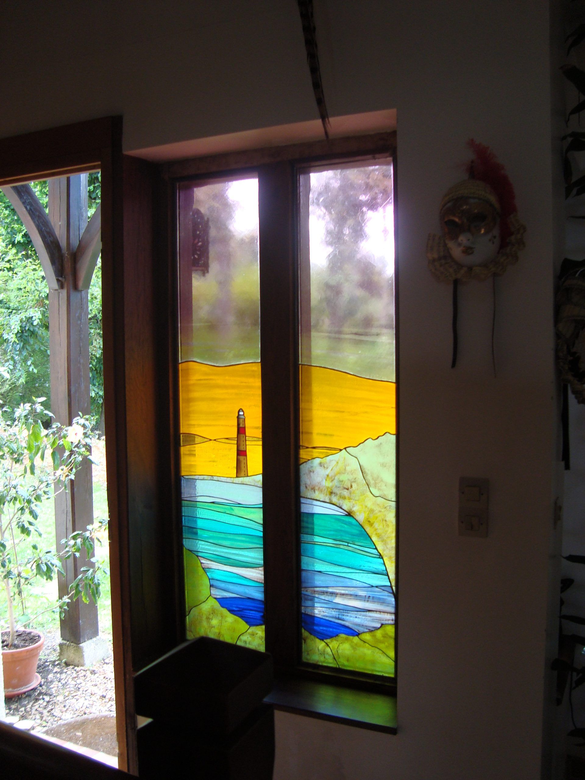Vitrail représentant un paysage jaune et bleu, flanqué d'une porte. Un masque décoratif est accroché à proximité.
