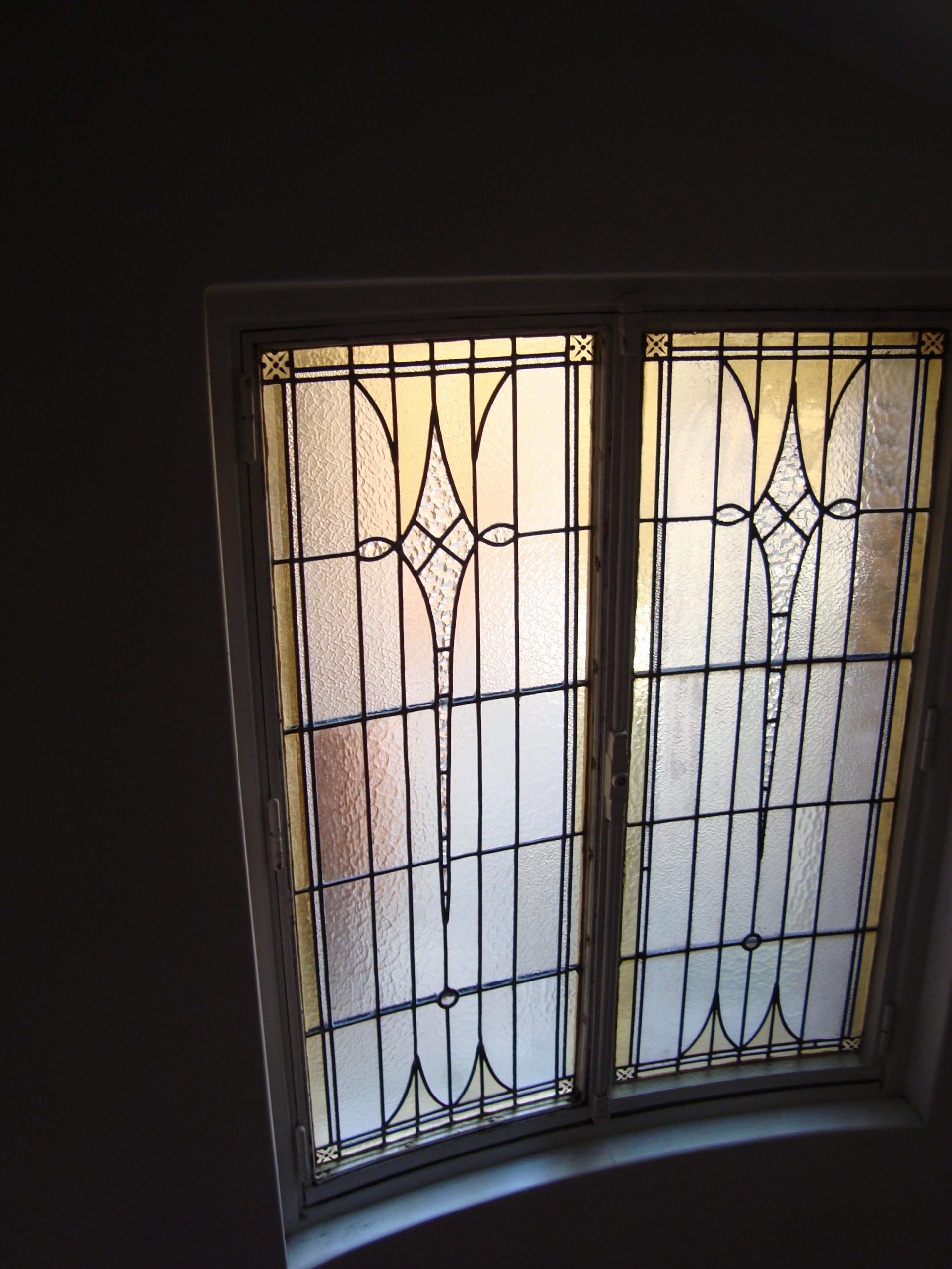 Vitrail orné de fines barres de métal noir et de verre dépoli. Une douce lumière le traverse.