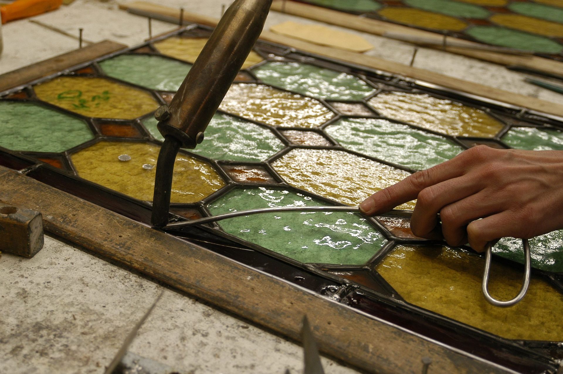 Personne soudant les fils de plomb d'un panneau de vitrail, avec du verre jaune et vert.