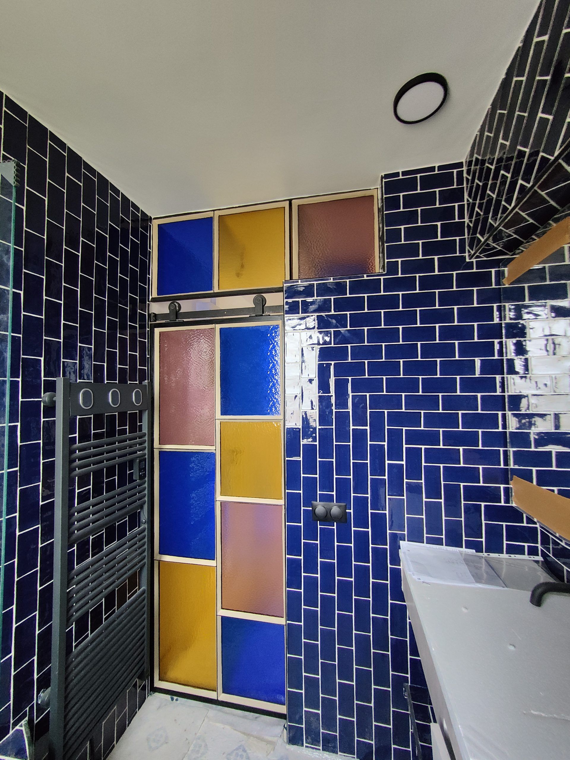 Salle de bains carrelée de bleu avec une porte de douche en vitrail.