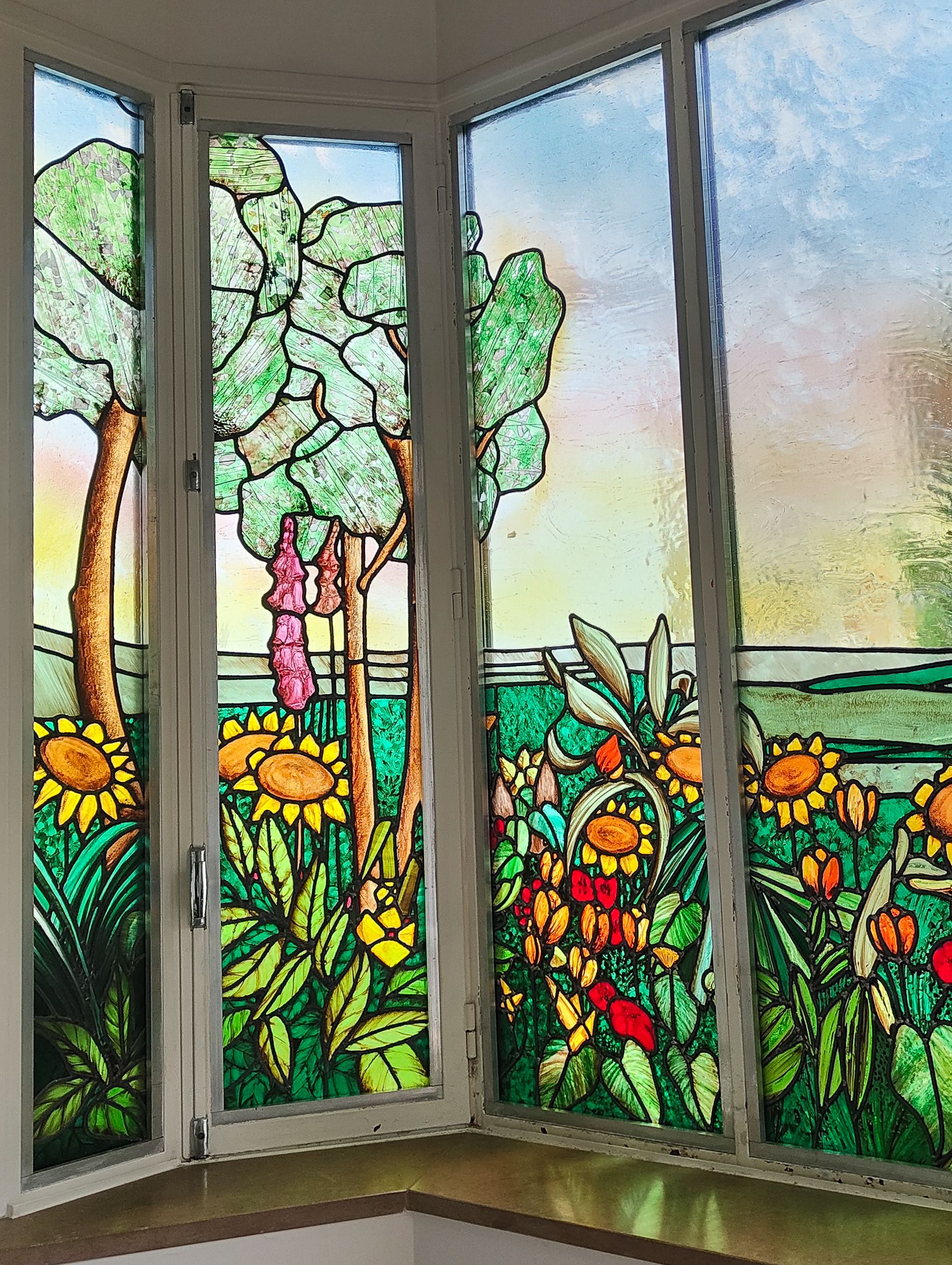 Vitrail représentant un jardin luxuriant avec des tournesols, des arbres et une figure d'enfant.