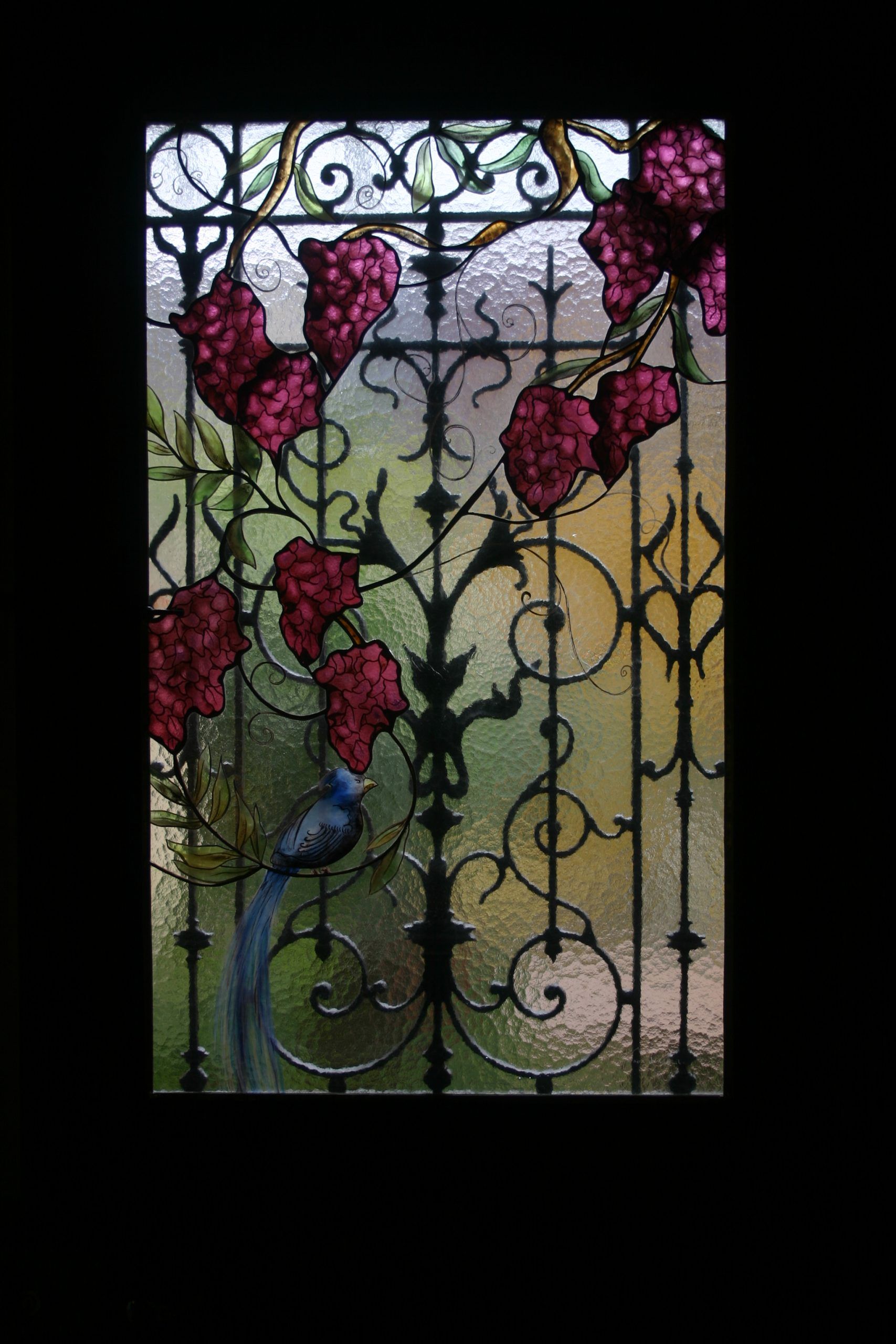 Vitrail orné de fleurs rouges et d'un oiseau bleu sur une structure métallique noire, le tout sur fond jaune-vert.