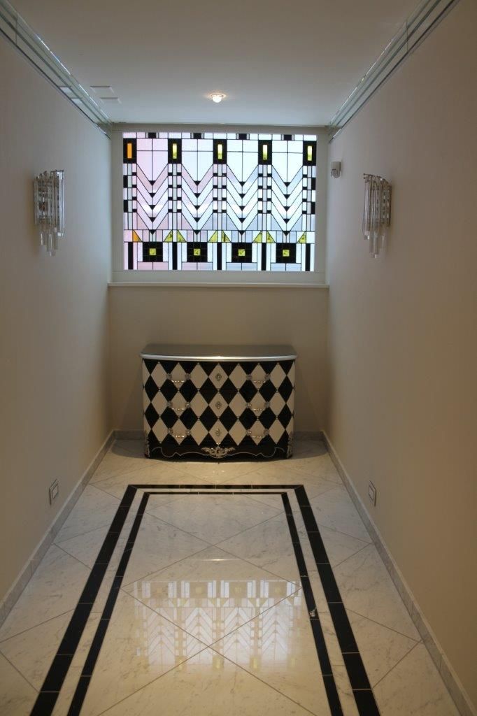 Couloir avec commode à losanges noirs et blancs, fenêtre décorative et appliques.