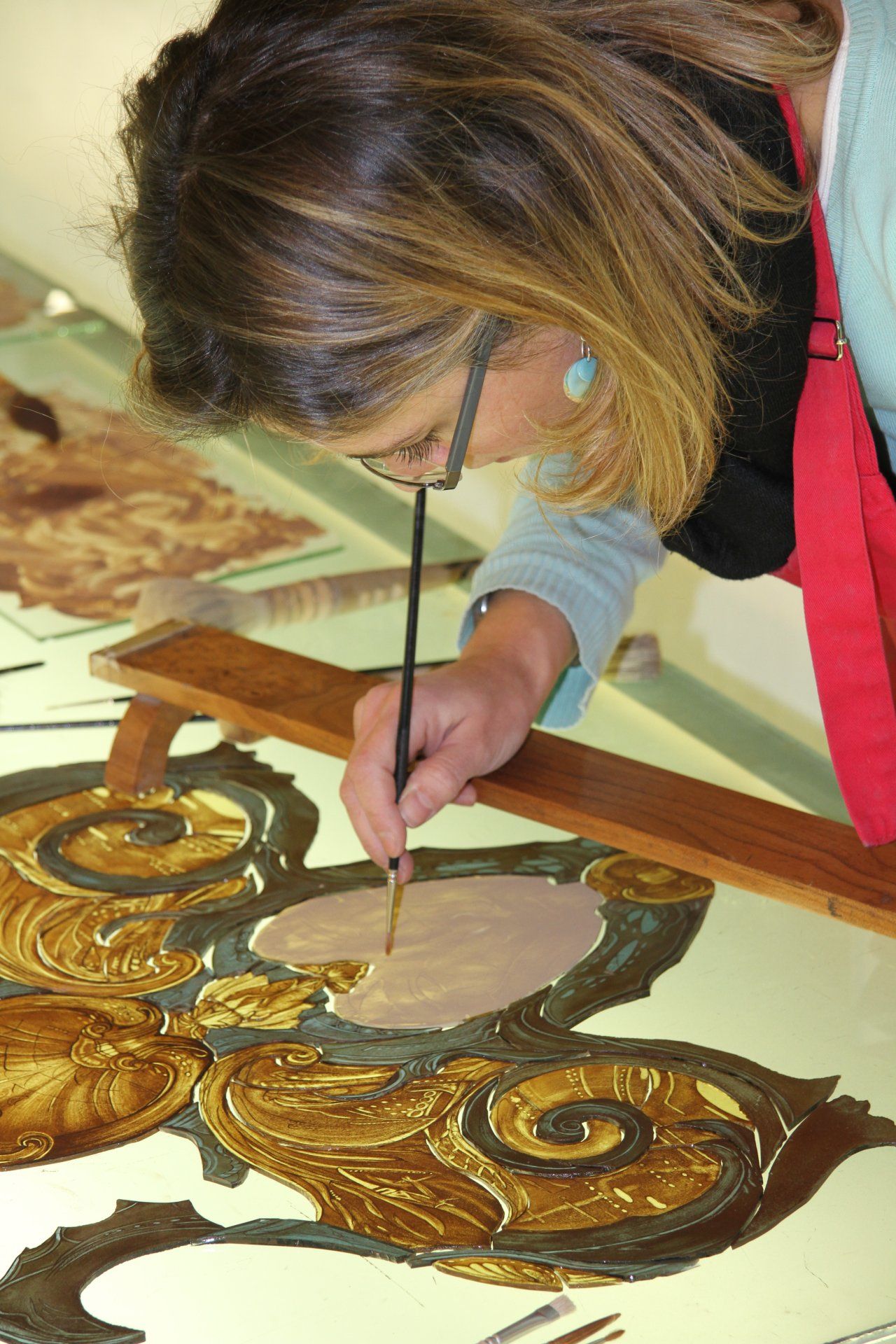 Une femme portant des lunettes peint un motif doré avec un pinceau fin sur une surface plane.