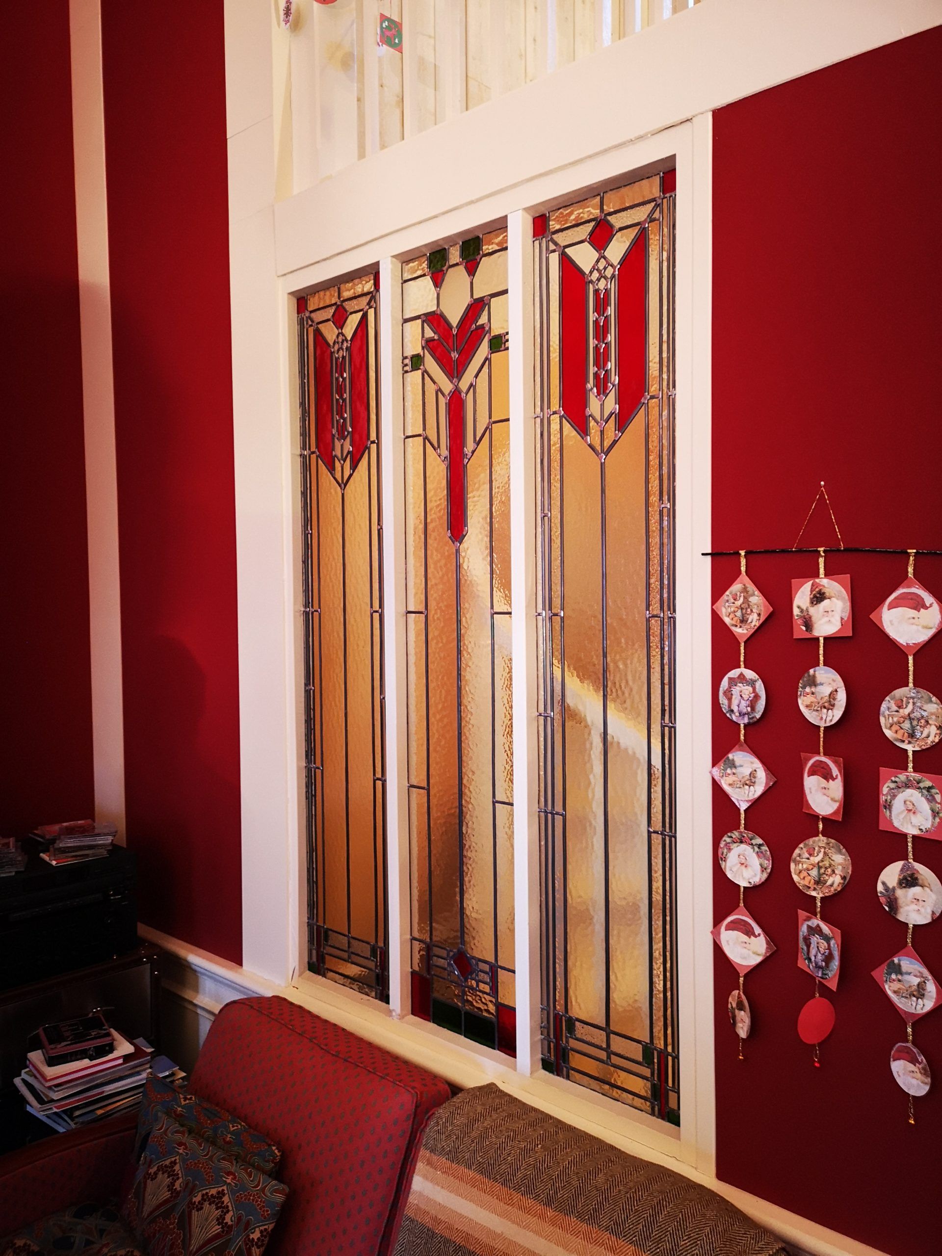 Vitrail à motifs géométriques rouges et or sur fond de murs rouges. Objets décoratifs accrochés au mur.