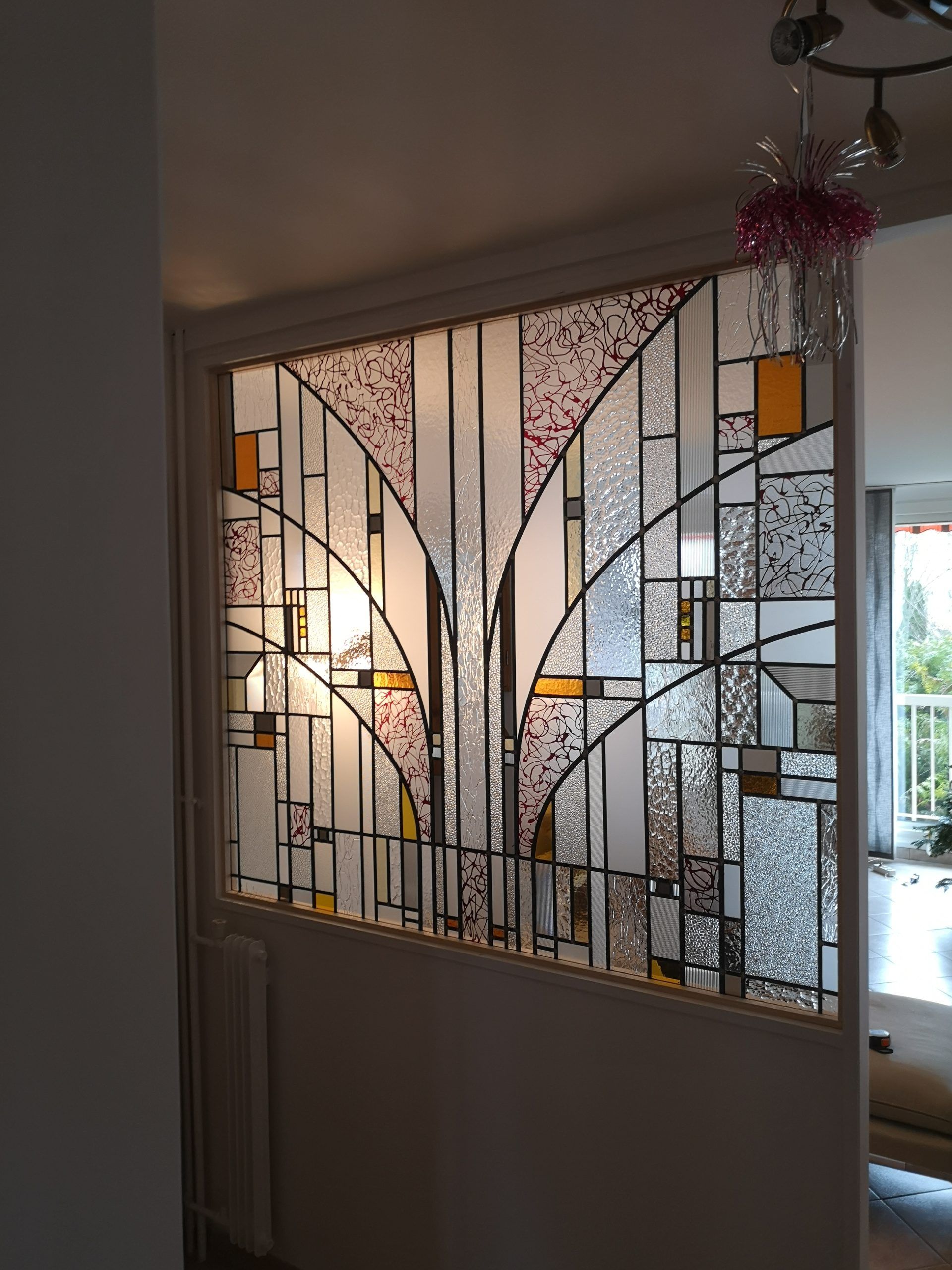 Paravent en vitrail, motif géométrique avec panneaux texturés ambrés, roses et transparents, lignes noires, illuminé.