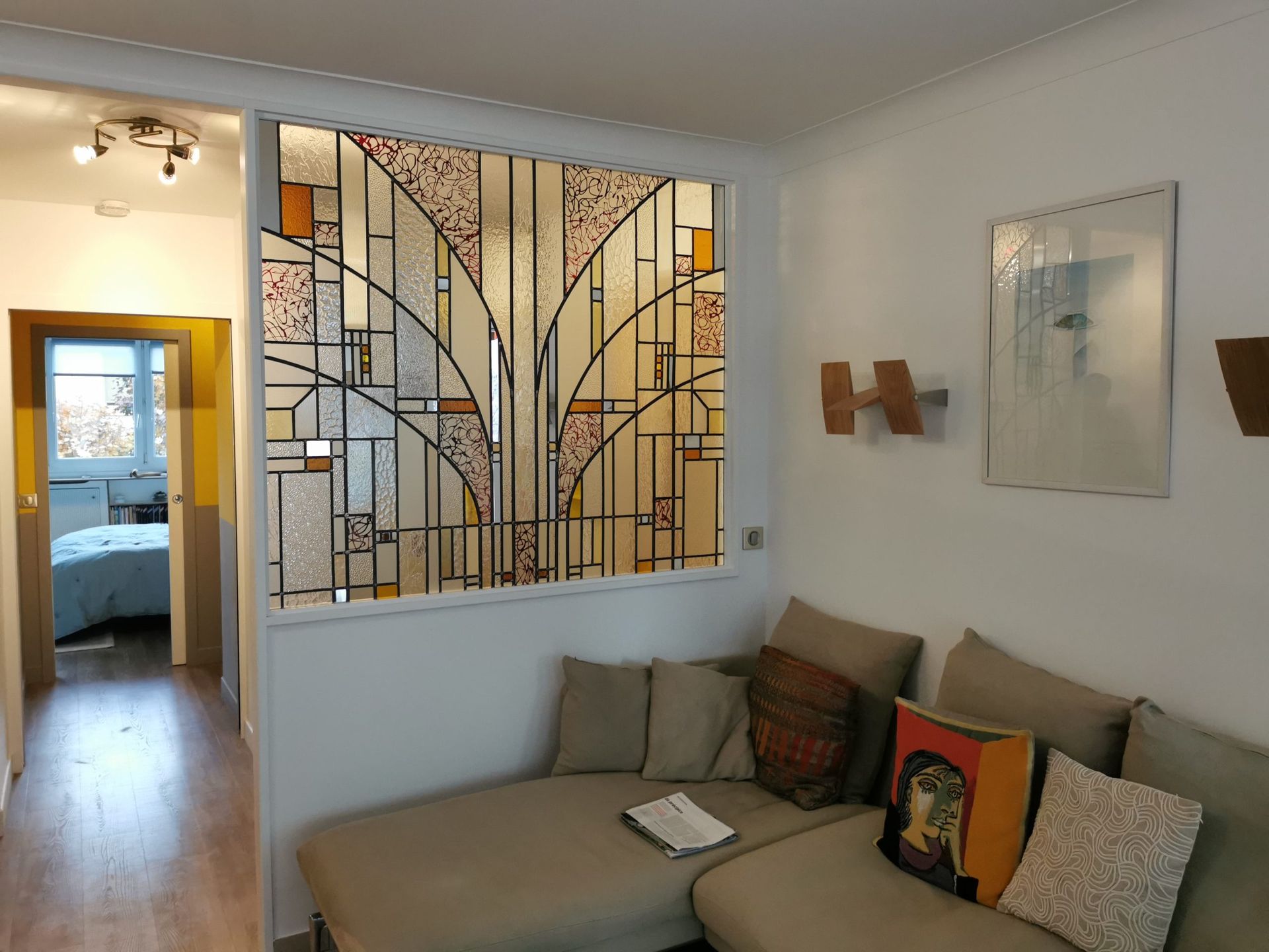 Salon avec canapé beige, vitrail et couloir.