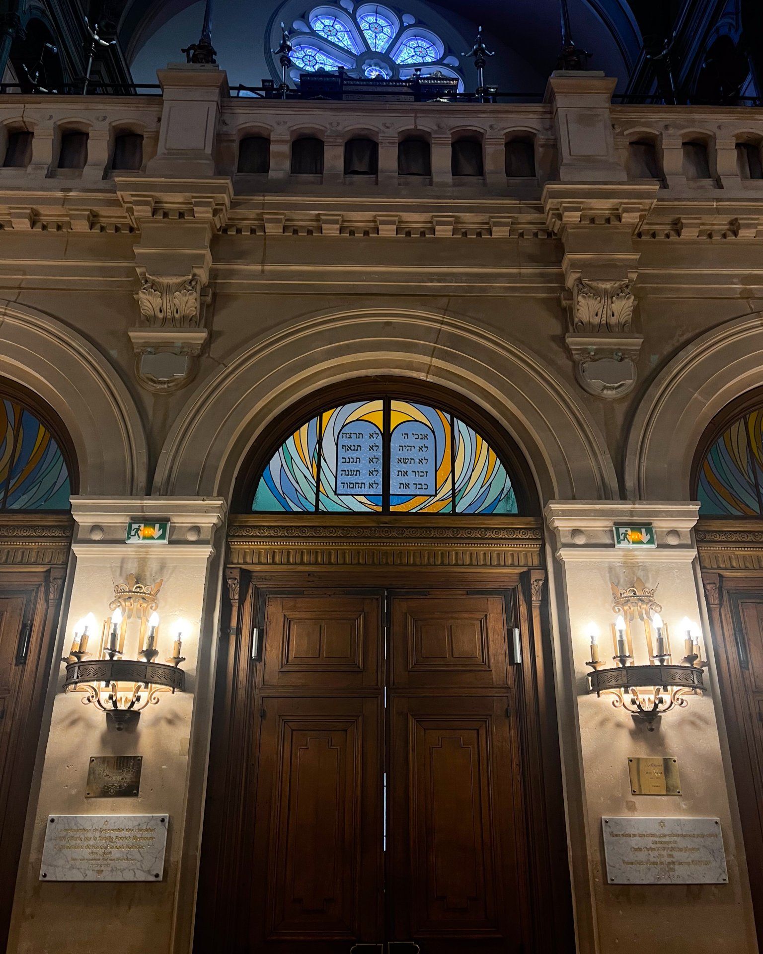 Entrée de synagogue ornée avec portes en bois, vitraux au-dessus et éclairage extérieur.
