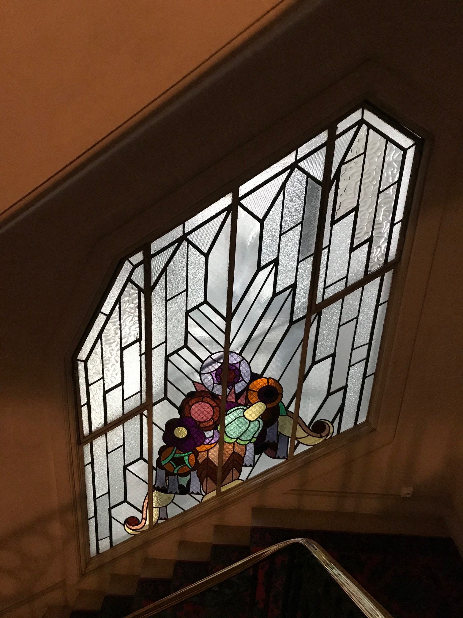 Vitrail à motifs géométriques et floraux, placé au-dessus d'un escalier.