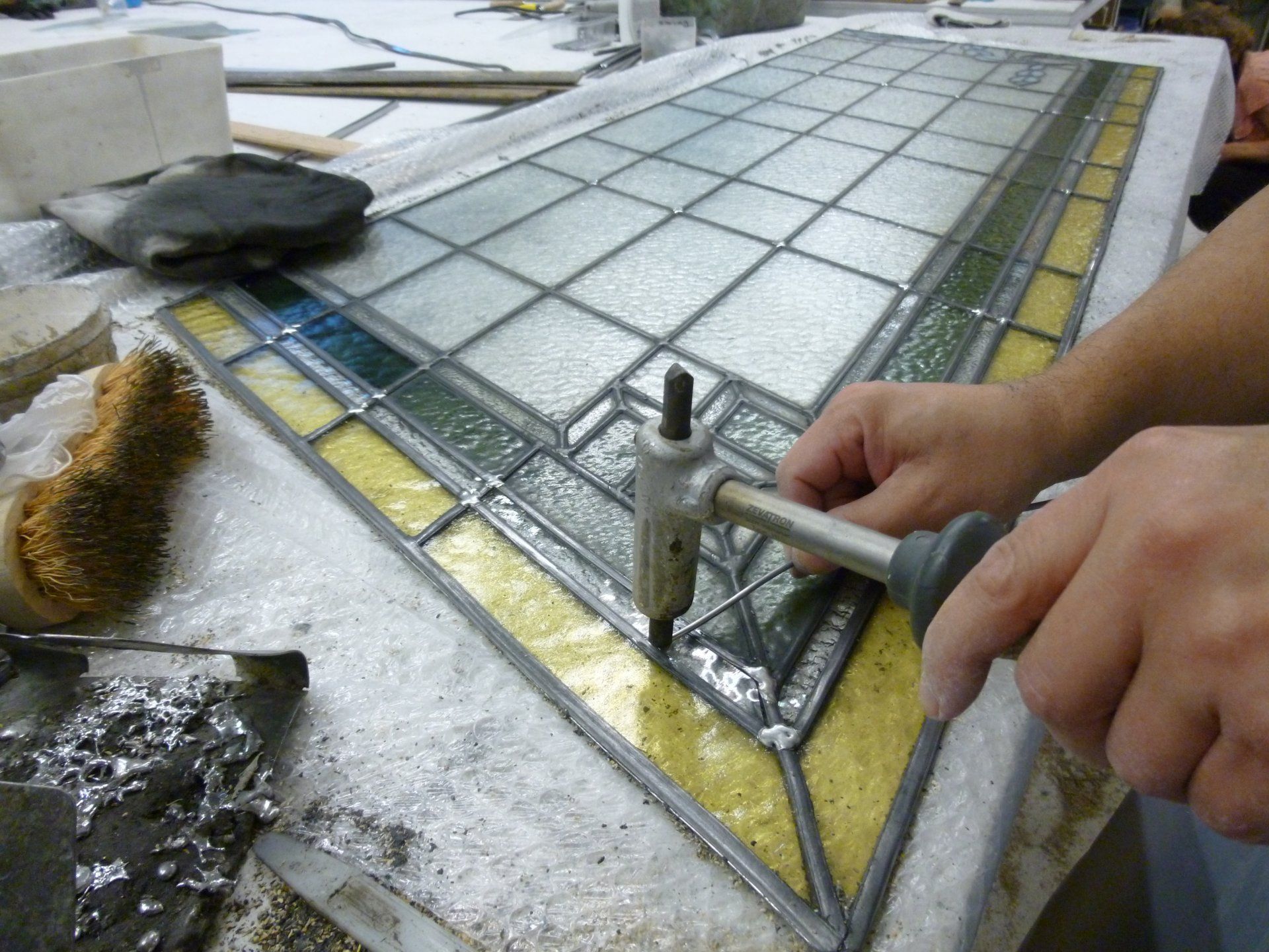 Gros plan d'une personne utilisant un outil de soudure sur un panneau de vitrail.