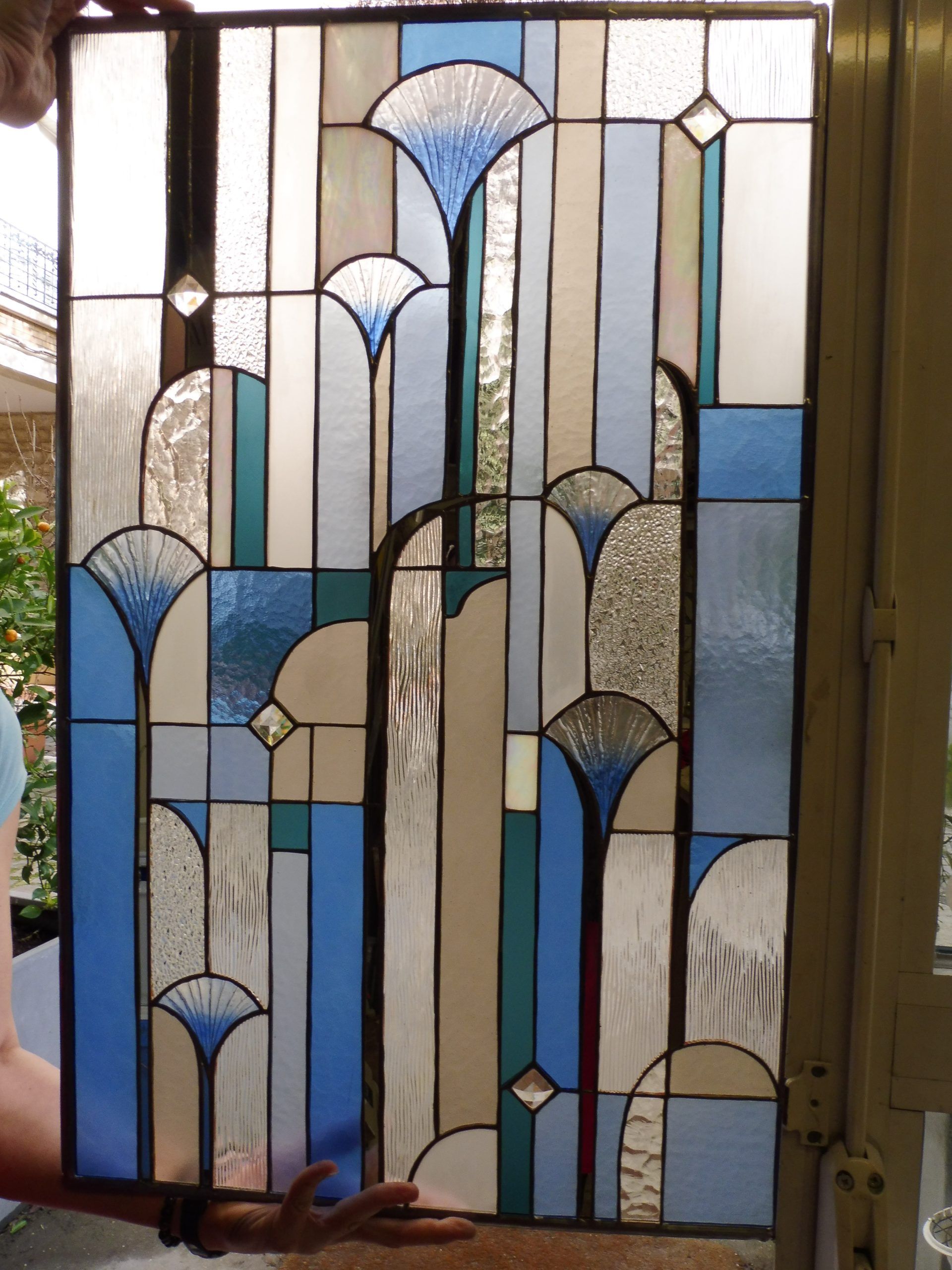 Panneau de vitrail de style Art déco dans les tons bleus, blancs et turquoise, tenu par des mains.