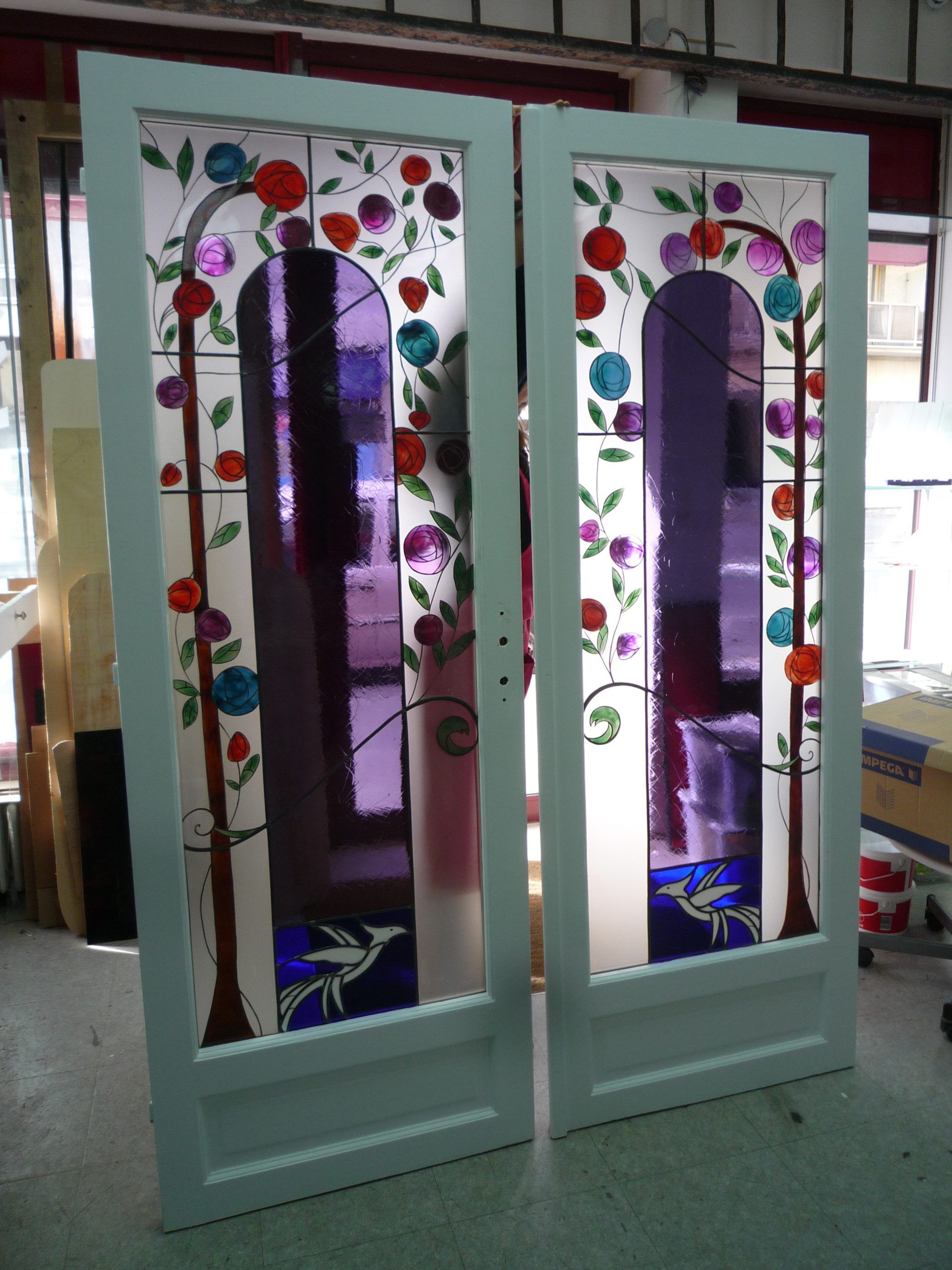 Deux portes à cadre blanc ornées de vitraux. Motifs floraux violets, bleus, oranges et rouges.
