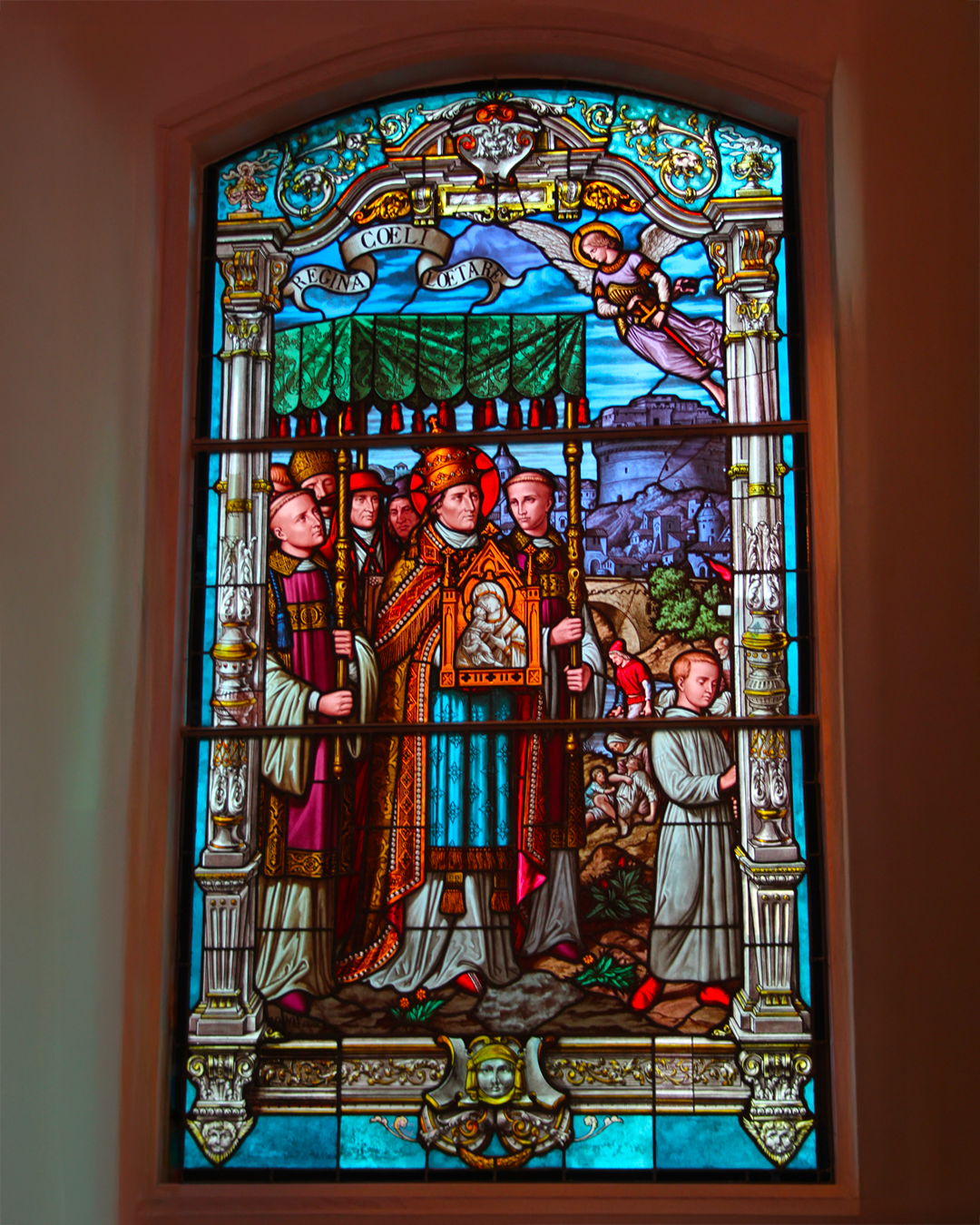 Vitrail représentant une scène religieuse : une procession avec des personnages en robes ornées, un ange et un édifice.