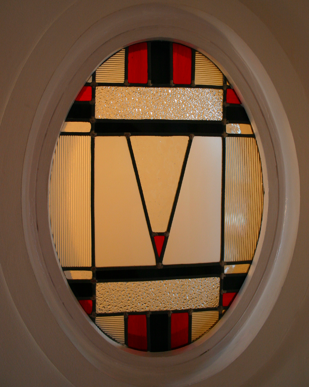 Vitrail ovale orné d'une forme géométrique blanche centrale et de touches de rouge, de noir et d'or.