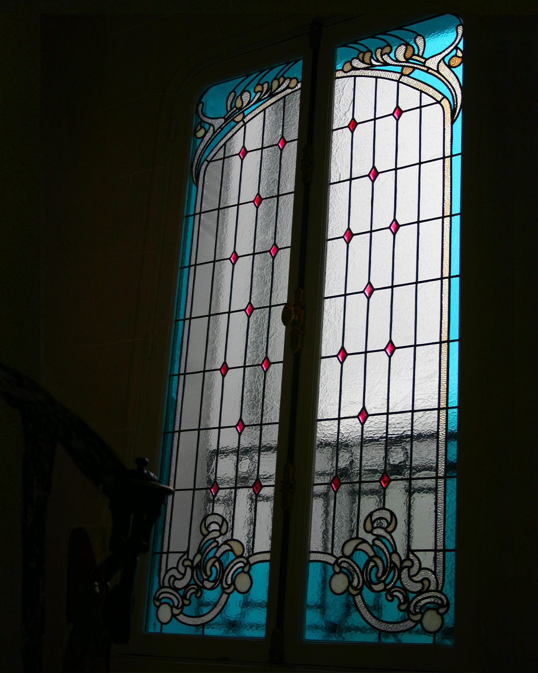 Vitrail orné de bordures turquoise, de motifs décoratifs et de détails en forme de losange rose.