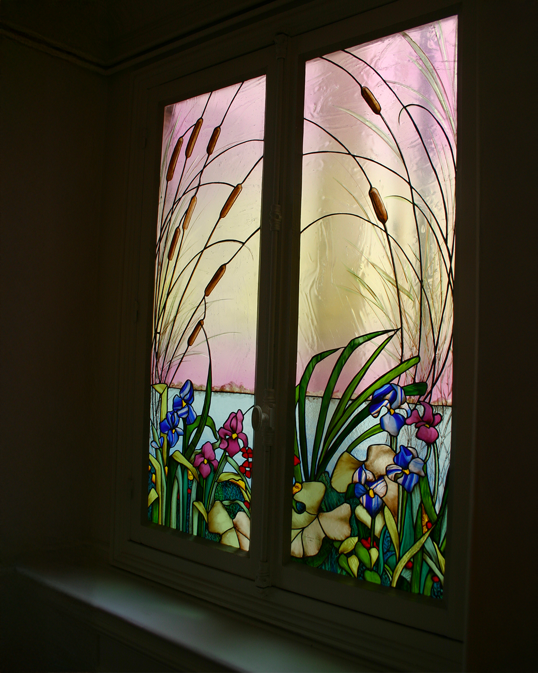 Vitrail représentant un étang avec des iris, des quenouilles et un ciel rose et jaune.