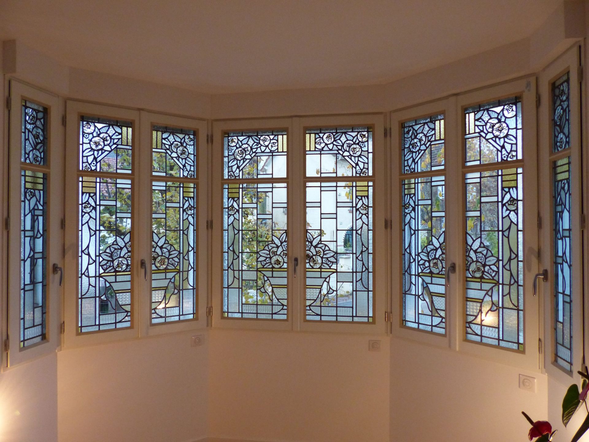 Fenêtre en baie avec cadres blancs et vitraux noirs et bleus aux motifs complexes.
