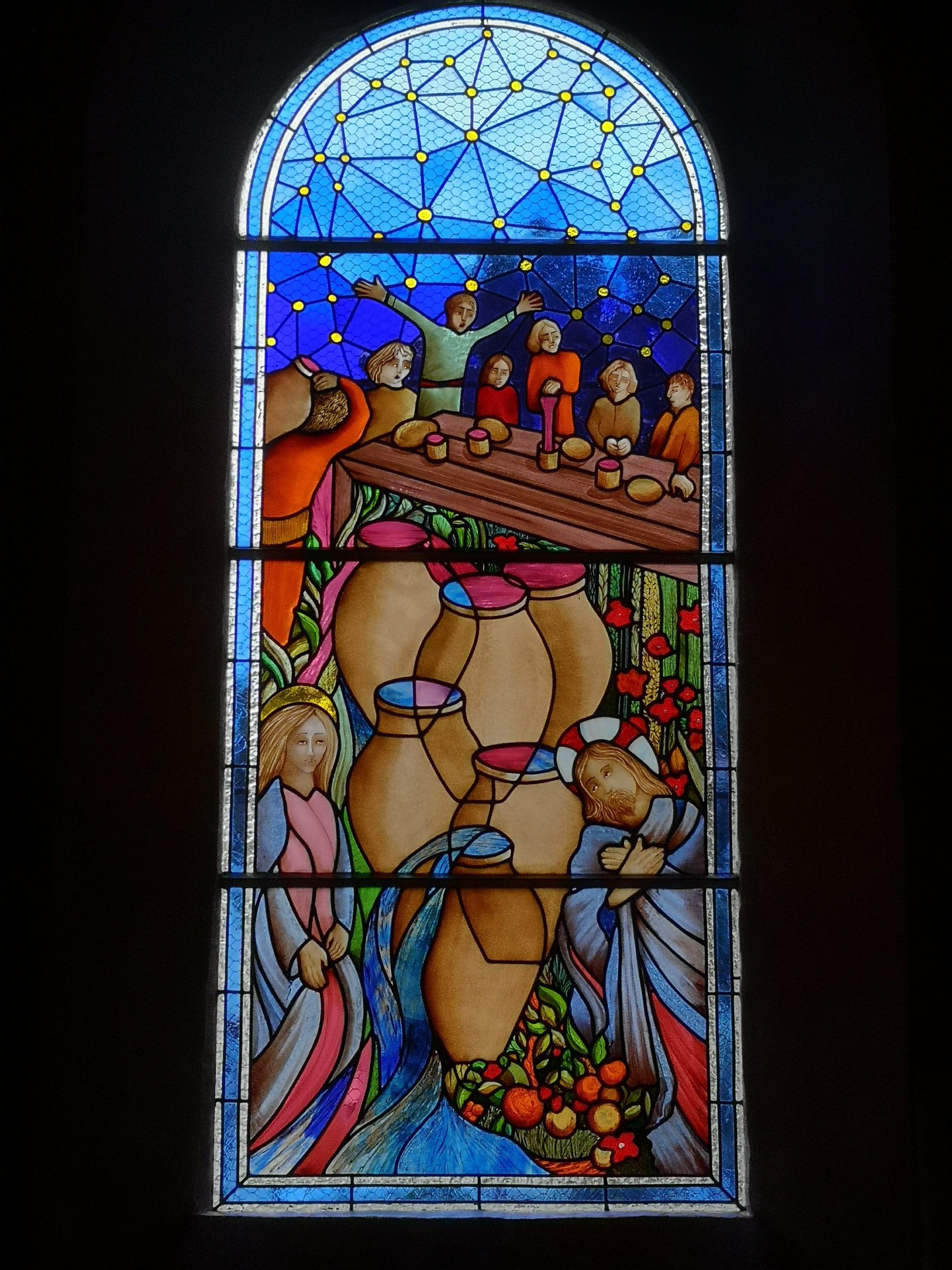 Vitrail représentant des personnages attablés à une table avec des jarres et un ciel bleu en arrière-plan.