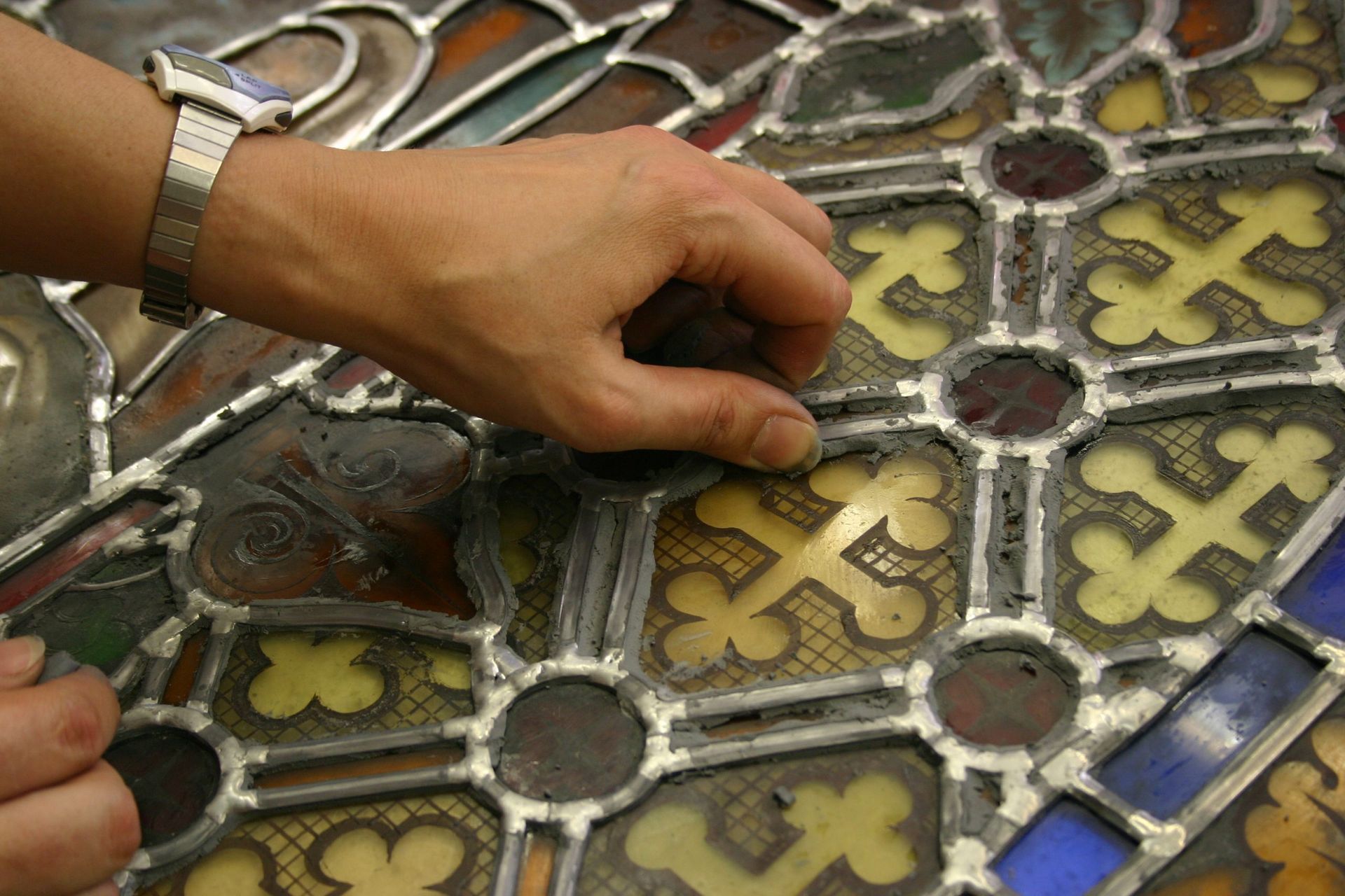 Restauration manuelle d'un vitrail, retouche délicate d'un motif en croix jaune et marron.