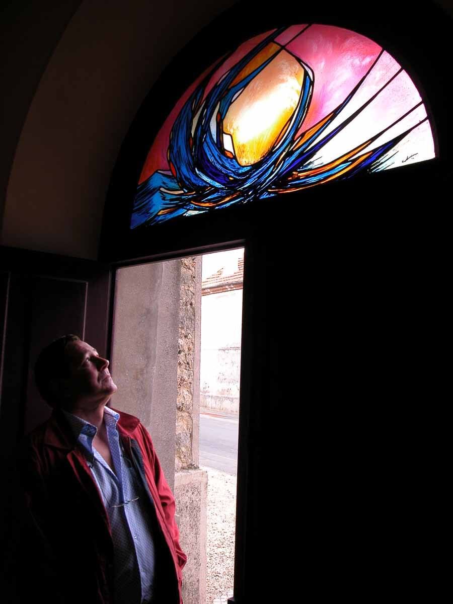 Un homme lève les yeux vers un vitrail coloré dans une arche ; la lumière le traverse.