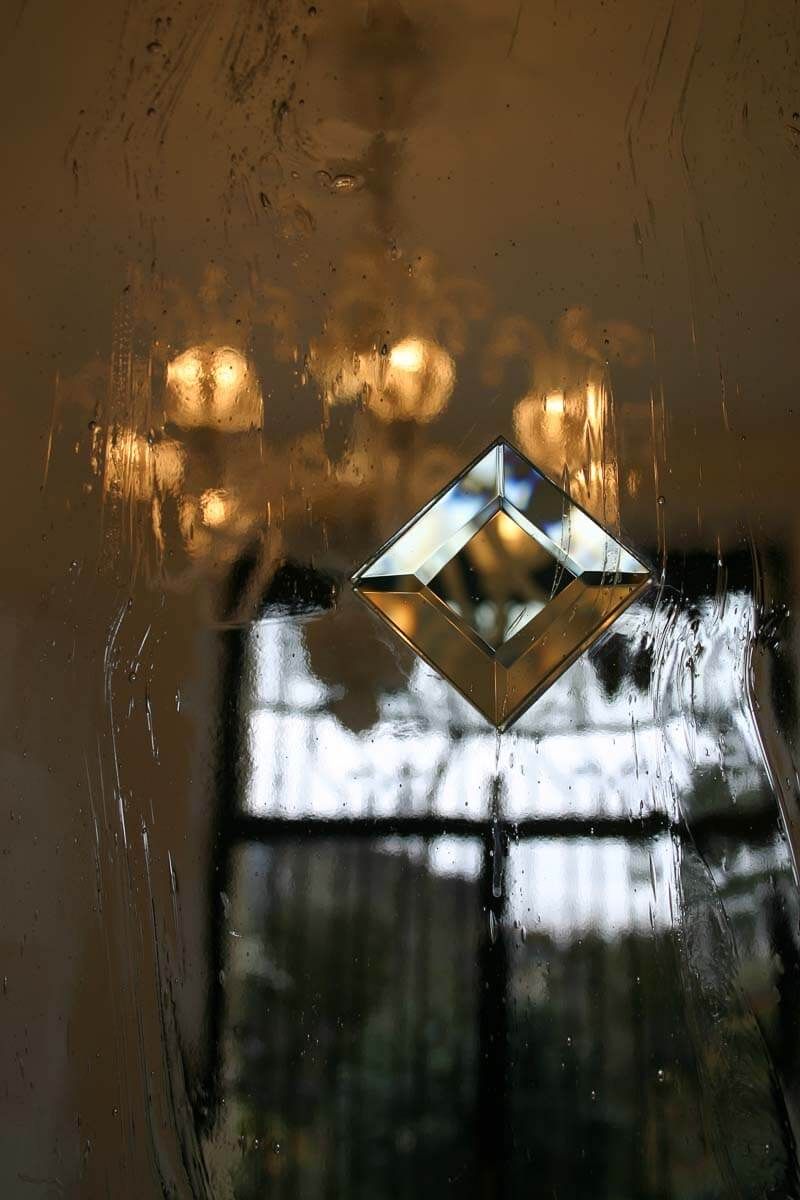 Décoration en verre en forme de losange sur une fenêtre reflétant un lustre et une fenêtre avec des rideaux.