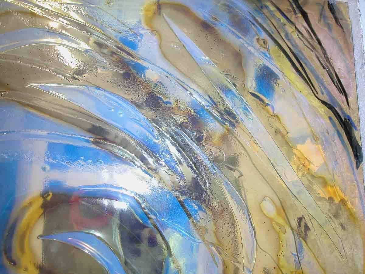 Vitrail abstrait aux formes fluides et translucides dans les tons bleus, jaunes et bruns, avec une surface réfléchissante et brillante.