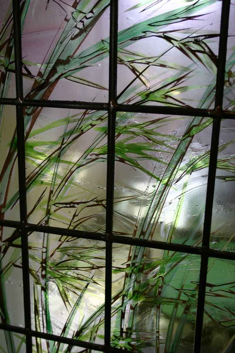 Vitrail représentant des tiges et des feuilles de bambou vertes sur fond translucide, encadré de lignes sombres.